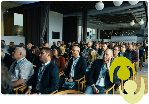 A group of people sitting in rows at an event, listening to a speaker