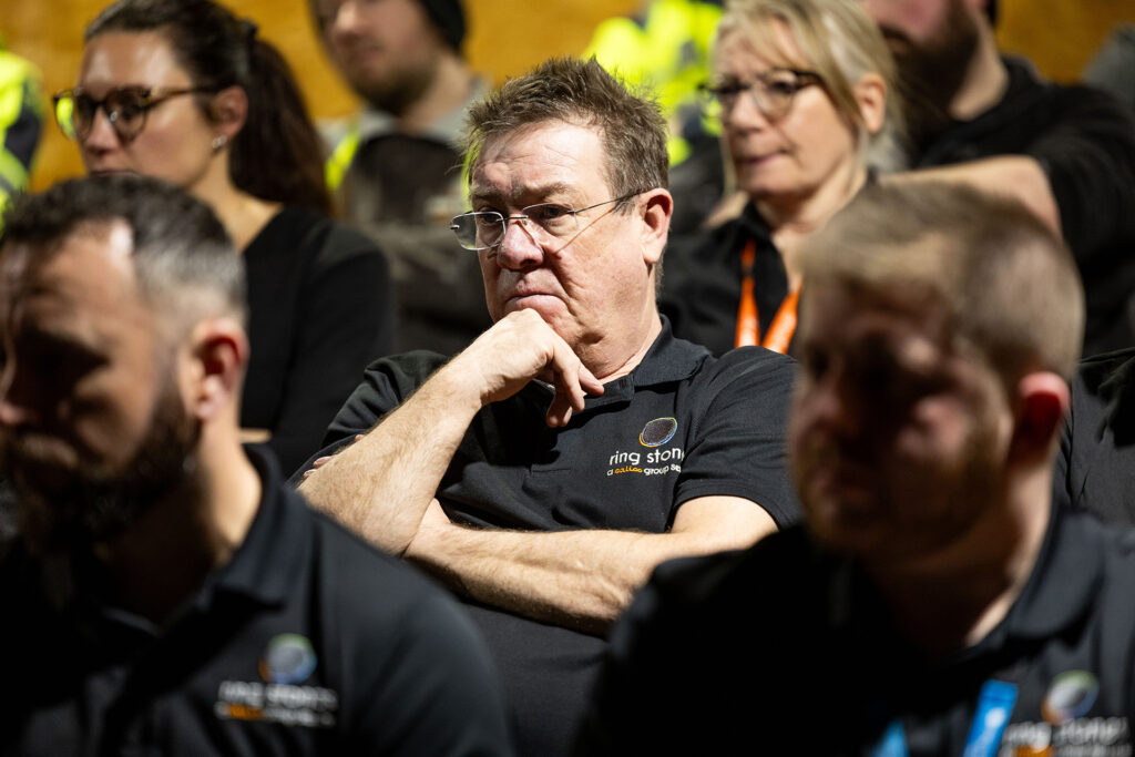 Adult learner seated in a group training session, wearing a work polo, listening during an in‑person course.